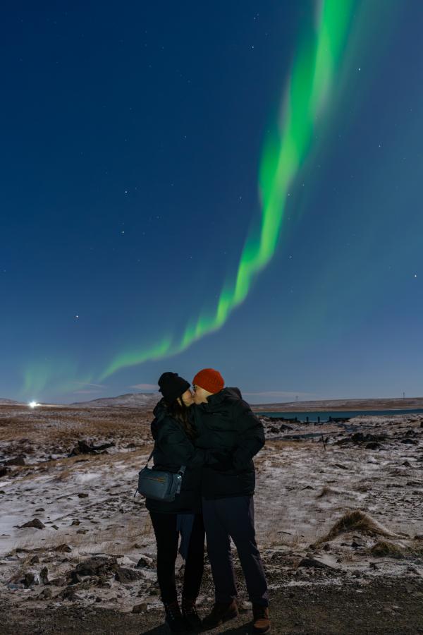 Couple kissing under the northern lights in a snowy Icelandic landscape at night
